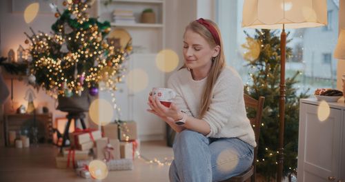 Portrait of woman holding christmas tree at home