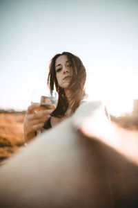 Young woman drinking water from glass against sky