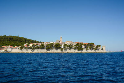 Buildings by sea against clear blue sky