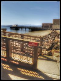 Walkway by sea against buildings in city against sky