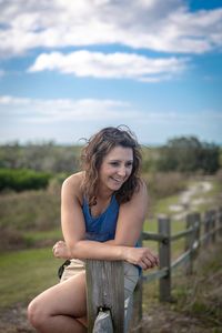 Young woman smiling while sitting on land against sky