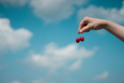 Close-up of hand holding strawberry against sky