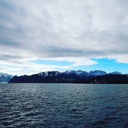 Scenic view of sea by snowcapped mountains against sky