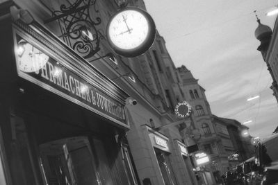 Low angle view of illuminated clock hanging against sky in city