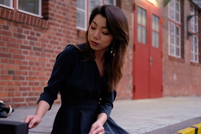 Full length of young woman standing against brick wall