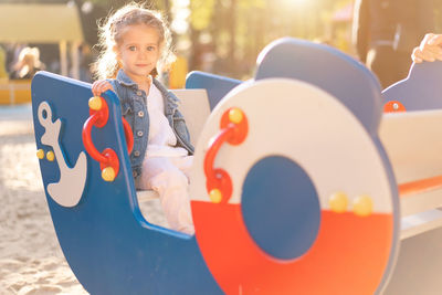 Portrait of girl sitting in play equipment at park on sunny day