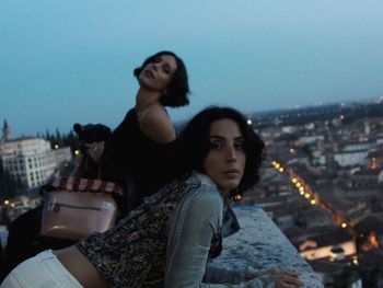 Portrait of female friends standing at building terrace against sky