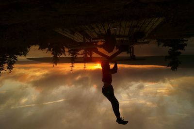 Upside down image of man performing headstand on table against lake during sunset