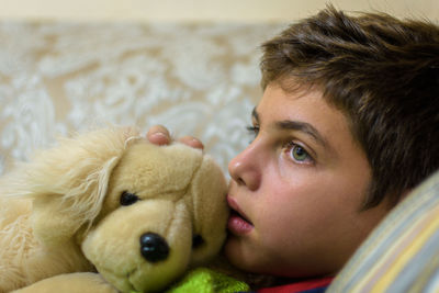 Thoughtful boy with stuffed toy looking away while relaxing on sofa at home