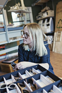 Female owner looking away while sitting on eyeglasses workshop