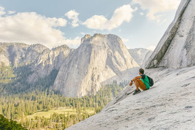 Man sitting on mountain against sky