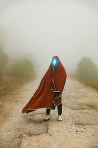 Young man with illuminated face standing on road wrapped in blanket