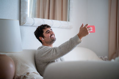Smiling man video calling while sitting on bed at home