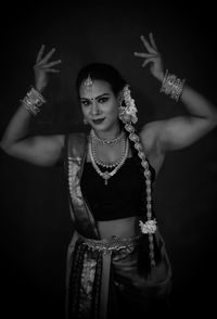 Portrait of young woman standing against black background