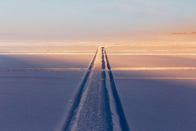 Tire track on snow covered field against sky