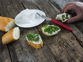 Cropped hand of person holding fresh bruschetta with feta cheese and chopped herbs wooden table