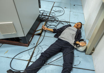 Shocked man holding cables while lying on floor by fuse box