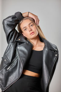 Portrait of young woman standing against white background black jacket