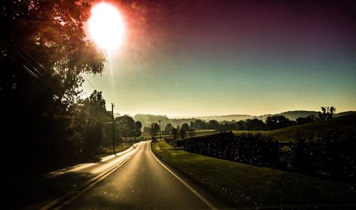 Road amidst trees against sky during sunset