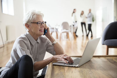 Senior businesswoman talking on mobile phone while using laptop