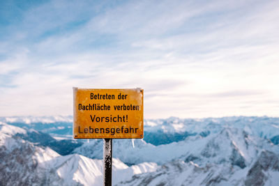 Close-up of road sign by snowcapped mountains against sky