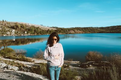 Portrait of young woman standing by lake against sky