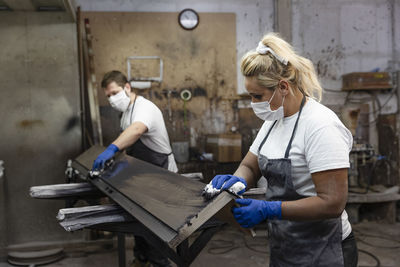 Carpenters applying varnish on wood with cloth while standing in factory