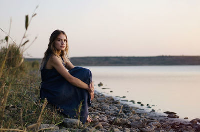 Young woman sitting on land against sky during sunset