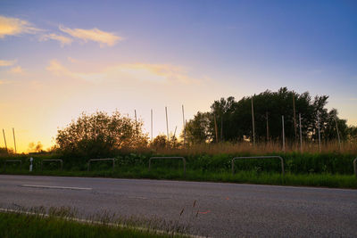 Road by trees on field against sky at sunset