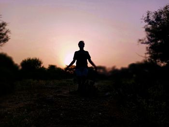 Silhouette man standing on field against sky during sunset