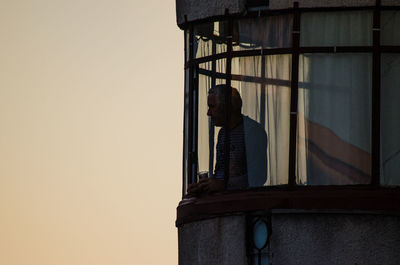 Rear view of man standing by building against clear sky