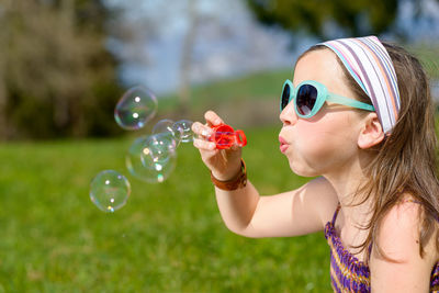 Teenage girl wearing sunglasses and hat while blowing bubbles at park