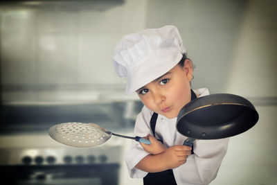 Portrait of girl wearing chef uniform holding kitchen utensils