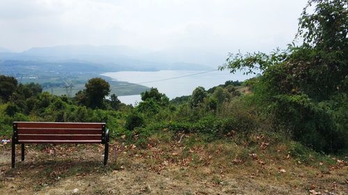 Empty bench in park against sky