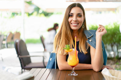 Young woman with drink sitting at sidewalk cafe