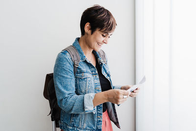 Woman holding smart phone while standing against wall