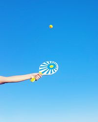 Cropped image of hands playing tennis against clear blue sky