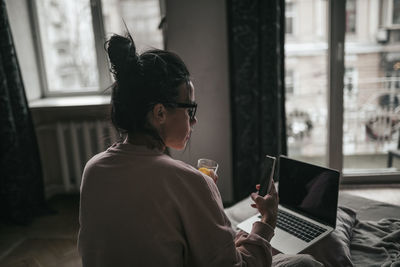 Woman using mobile phone while sitting on window