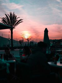 Silhouette people sitting in city against sky during sunset