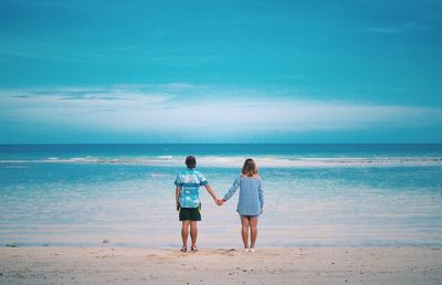 Rear view of women standing on beach against sky