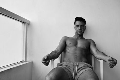 Portrait of shirtless mid adult man sitting on chair against wall