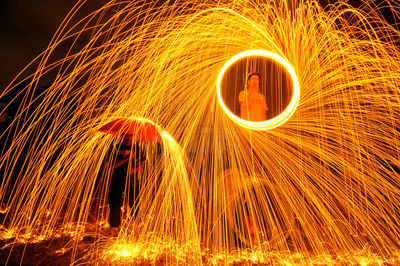 Men standing by spinning wire wool on field at night