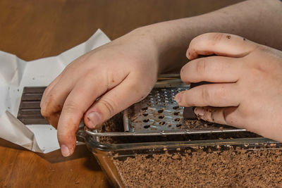 Cropped hands woman grating chocolate in container while sitting at home