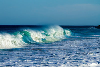 Waves splashing in sea against clear sky