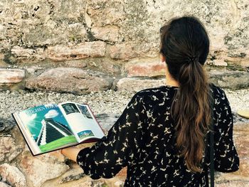 Rear view of woman reading book against wall