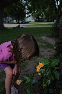 Girl smelling flower growing on plant at park