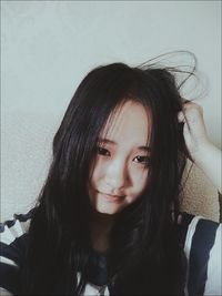 Close-up of girl with hand in hair against wall at home