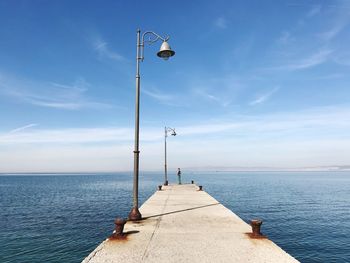 Man standing on pier by sea against blue sky