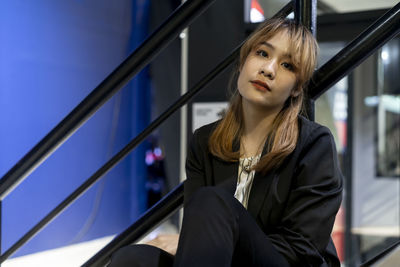 Portrait of businesswoman sitting against railing