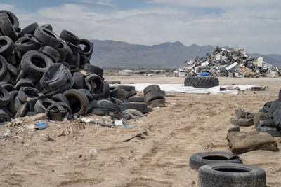 Stack of garbage on sand at beach against sky